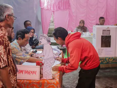 Calon pemilih mendaftar ke petugas Kelompok Penyelenggara Pemungutan Suara (KPPS) saat akan mencoblos di TPS 45 Kebon Pala, Jakarta, Rabu (17/5). TPS tersebut mengambil tema suasana pernikahan adat Jawa untuk menarik minat pemilih dan menekan angka golput. (Liputan6.com/Faizal Fanani)