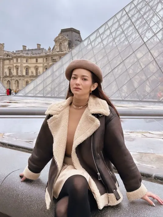 Lihat cantiknya inspirasi holiday look dari Enzy Storia. Dalam foto ini, ia berpose di depan bangunan ikonis di Paris, mengenakan turtleneck cokelat sebagai innerwear, yang ditumpuknya dengan jaket, dipadu dengan rok bernuansa senada dengan jaketnya, serta stoking hitam. Tak lupa ia menambahkan sentuhan aksesori berupa topi sebagai pemanis yang sempurna untuk keseluruhan tampilannya. Foto: Instagram.