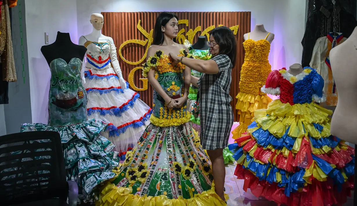 Dalam foto yang diambil pada tanggal 12 September 2024 ini, Leonora Buenviaje (kanan) menyiapkan gaun yang terbuat dari bahan daur ulang untuk Maria Theresa Deligero (kiri), di rumahnya di Cainta, provinsi Rizal, Filipina. (JAM STA ROSA/AFP)