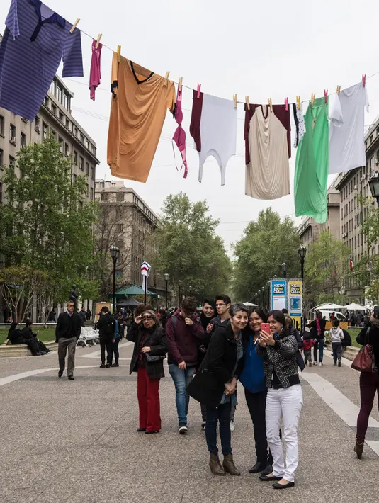Pengunjung berswafoto di bawah seni instalasi jemuran pakaian raksasa di Paseo Bulnes, Santiago (2/10). Instalasi yang mirip jemuran tersebut bagian dari "Hecho en Casa Fest" (Made at Home Festival). (AFP Photo/Martin Bernetti)