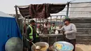 Dua relawan di dapur amal berdiri di dekat panci-panci besar saat mereka membagikan makanan kepada keluarga-keluarga Palestina yang mengungsi di kamp pengungsi Bureij, Jalur Gaza Tengah pada Senin 18 Mei 2026. (Eyad Baba/AFP)
