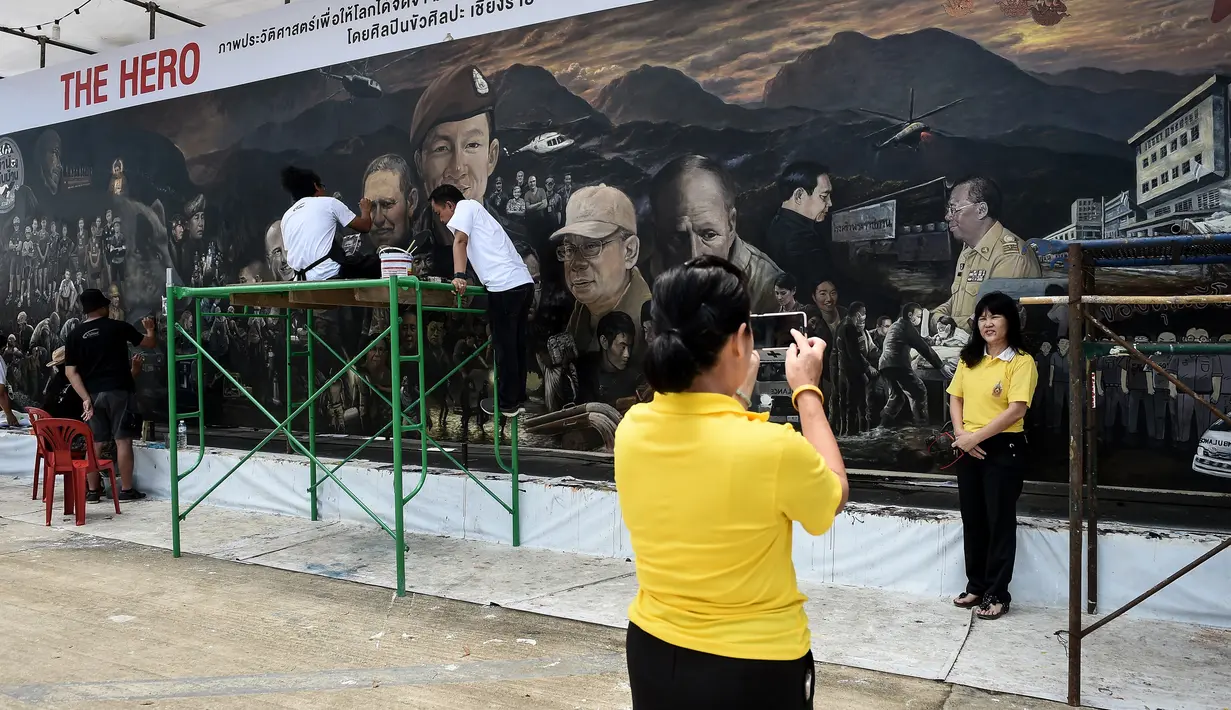 Pengunjung berfoto depan mural raksasa berjudul 'The Heroes' di Chiang Rai, Thailand, 18 Juli 2018. Mural itu untuk menghormati upaya penyelamatan 12 remaja dan pelatih sepak bola yang terperangkap di  gua lebih dari dua minggu. (AFP/Lillian SUWANRUMPHA)