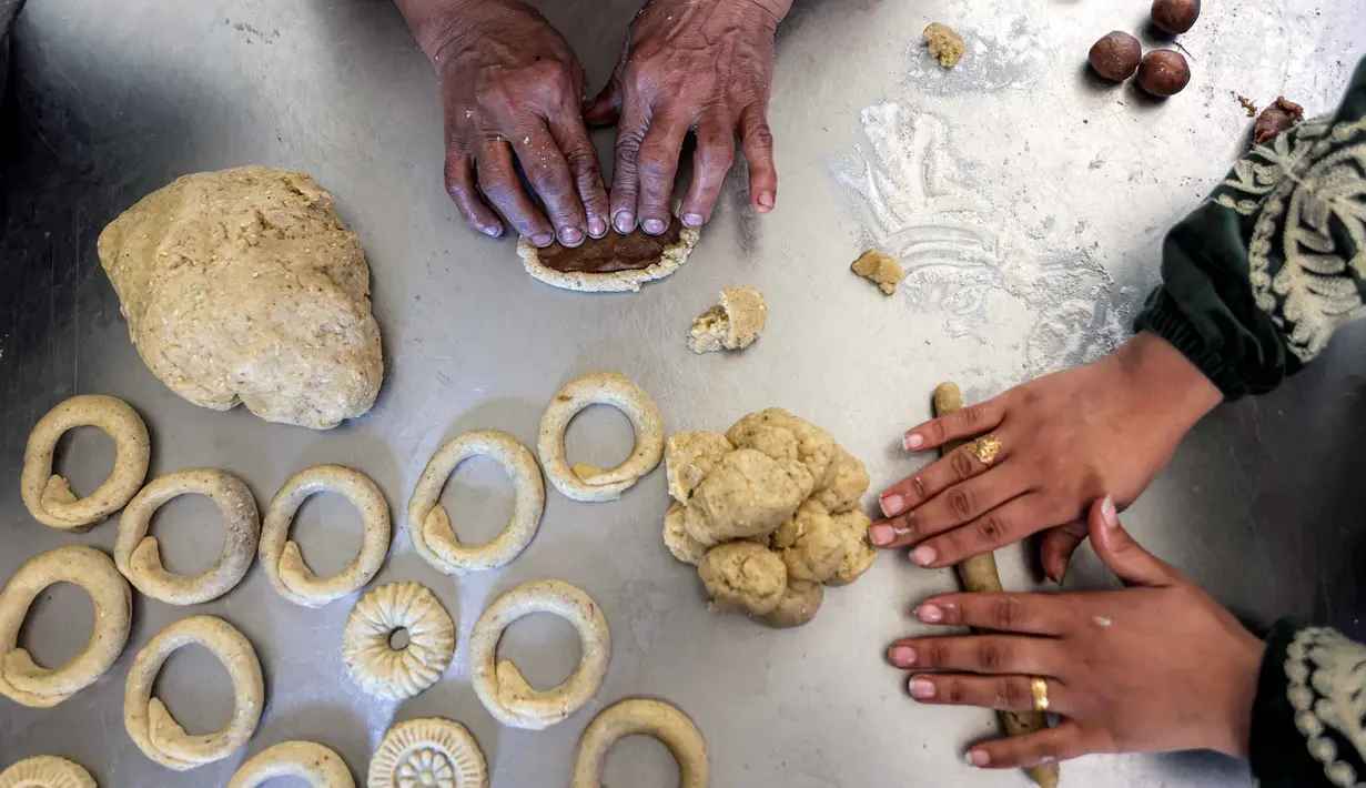 Akan tetapi ciri khasnya yang berbentuk cincin dan dipenuhi taburan biji wijen tetap ada di berbagai wilayah berbeda. Tampak dalam foto, para wanita menyiapkan biskuit tradisional "kaak" yang berbentuk cincin menjelang Idul Fitri, hari raya yang menandai berakhirnya bulan puasa suci Ramadan, di Kota Gaza pada 16 Maret 2026. (Omar AL-QATTAA/AFP)