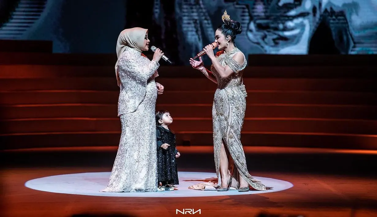 Kris Dayanti mengenakan halter dress berhiaskan payet berkilauan nuansa emas yang mewah. Di sisi kirinya, Aurel Hermansyah mengenakan cape dress berhiaskan payet dari Julianto Official.  [Instagram/aurelie.hermansyah]