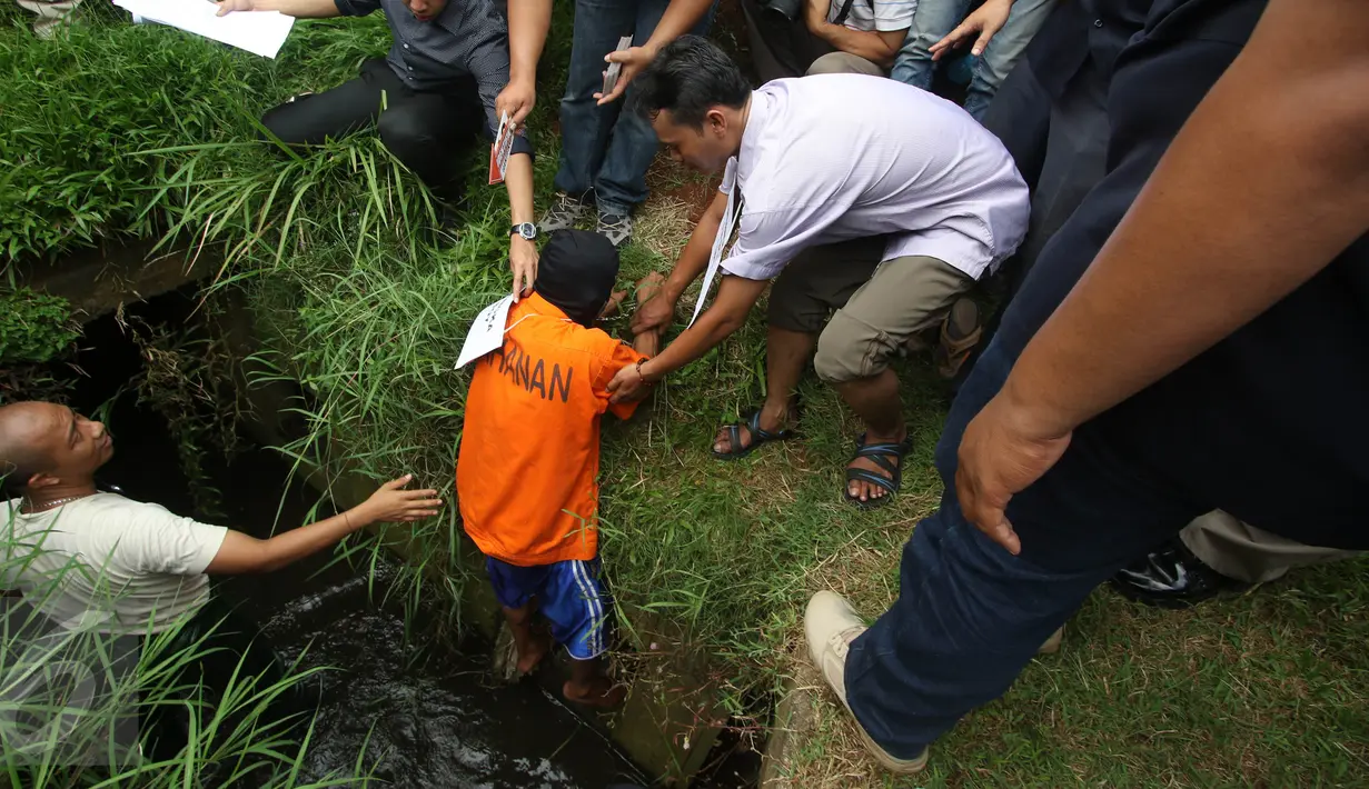 Petugas membantu tersangka pada rekonstruksi pencurian kabel gorong-gorong di Jalan Medan Merdeka Selatan, Jakarta, Selasa (15/3). Tersangka memperagakan cara masuk ke dalam lubang gorong-gorong dan cara mencuri kabel. (Liputan6.com/Immanuel Antonius)