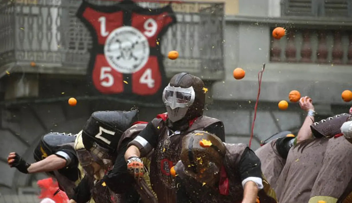 Sejumlah orang yang mengenakan helm melemparkan jeruk kepada warga sebagai bagian dari tradisi "perang jeruk" yang diselenggarakan selama Karnaval Ivrea di Turin, Italia (16/2). (AFP PHOTO/Olivier MORIN)
