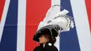 Seorang wanita mengenakan topi atau fascinator unik bermotif bulu melintas di depan bendera Union Jack saat menghadiri ajang pacuan kuda Royal Ascot di Ascot, Inggris, Selasa (18/6/2019). Royal Ascot menjadi ajang bagi wanita Inggris untuk tampil dengan fascinator unik. (AP Photo/Alastair Grant)