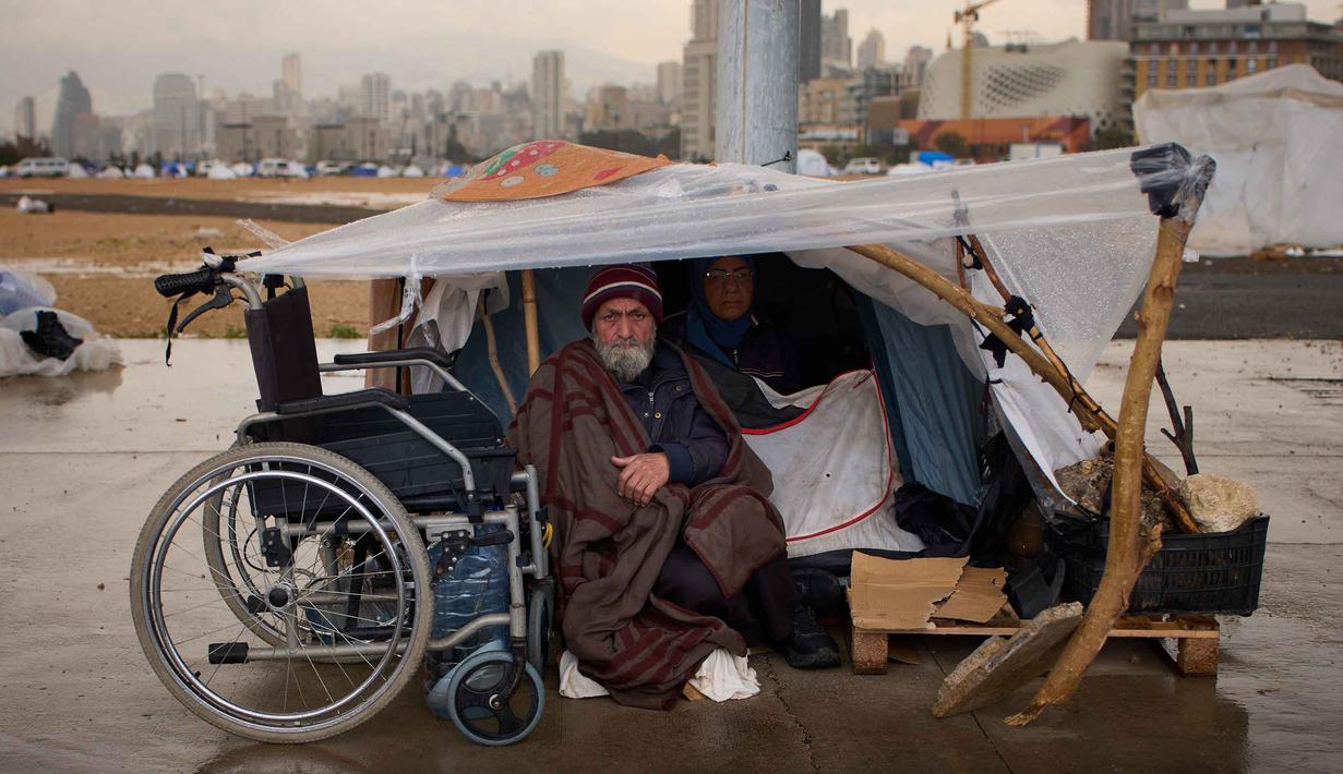 Situasi ini imbas eskalasi serangan udara Israel yang meluas di wilayah selatan, dan pinggiran Beirut, Lebanon. Tampak dalam foto, seorang pria bersama istrinya, yang mengungsi dari pinggiran selatan Beirut, Dahiyeh, berlindung dari hujan di dalam tenda di sepanjang pantai, Beirut, Lebanon, Kamis, 26 Maret 2026. (AP Photo/Emilio Morenatti)