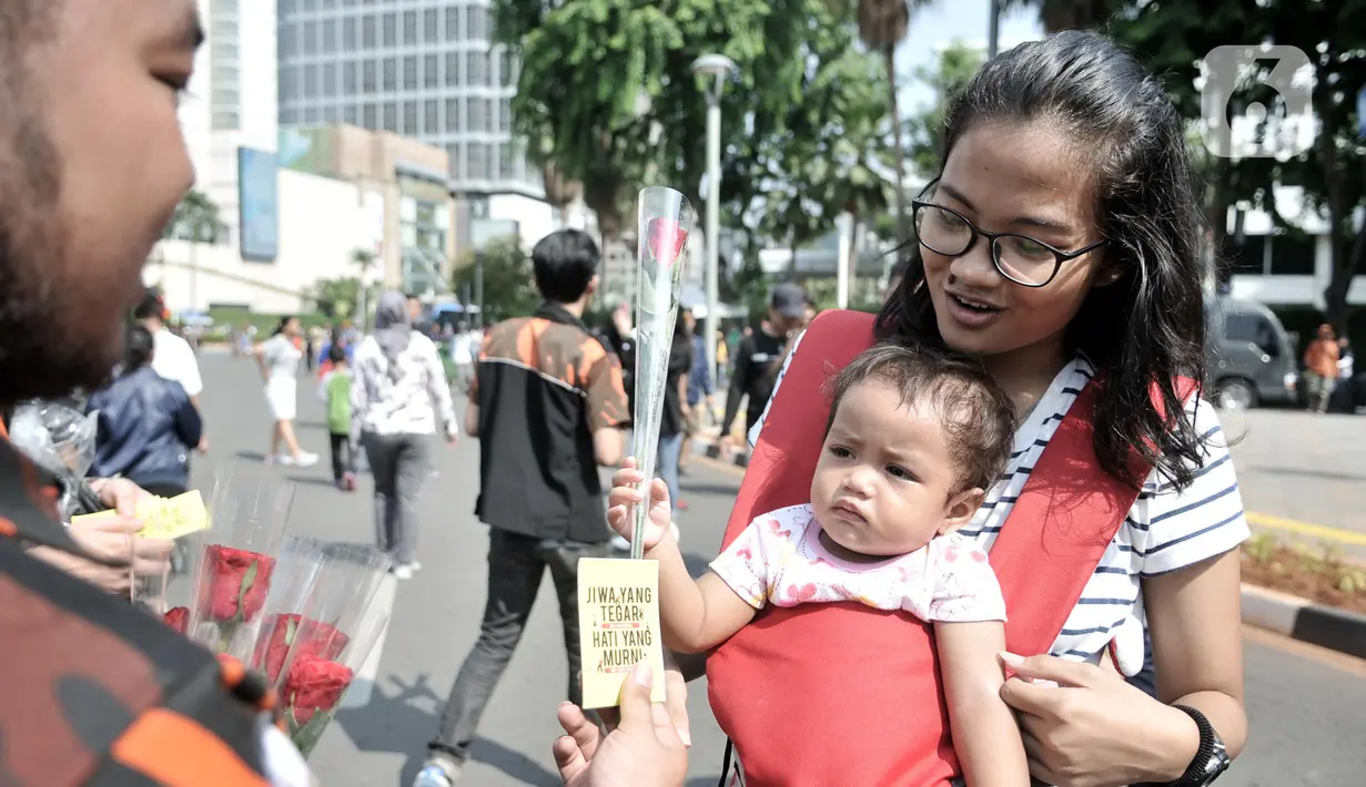 Aktivis memberikan bunga mawar dan buku panduan saat peringatan Hari AIDS Sedunia di Bundaran HI, Jakarta, Minggu (1/12/2019). Kegiatan ini bertujuan mengedukasi masyarakat tentang penyakit AIDS dan mengajak untuk peduli serta tidak menjauhkan penderita AIDS. (merdeka.com/Iqbal S. Nugroho)