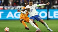 Pemain Timnas Prancis, Kylian Mbappe (kanan) berebut bola dengan pemain Timnas Belanda, Lutsharel Geertruida pada laga Grup B Kualifikasi Euro 2024 yang berlangsung di Stade de France, Sabtu (25/03/2023) WIB. Les Bleus menang dengan skor 4-0. (AFP/Anne-Christine Poujoulat)