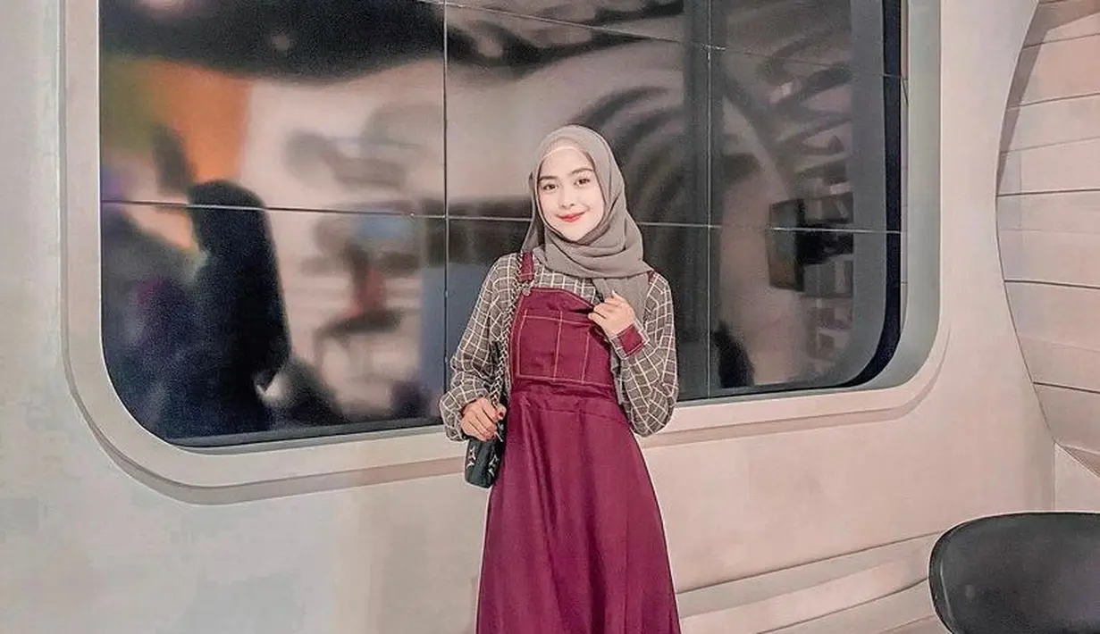 Gamis model overall warna merah kombinasi plaid long sleeve bikin tampilan terlihat manis. (Instagram/riaricis1795).