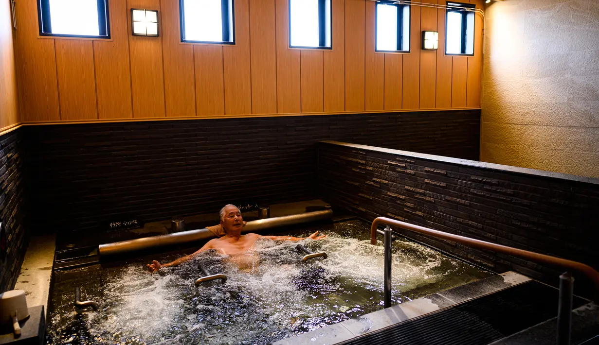 Seorang pria bersantai dalam kolam renang indoor di pemandian air panas Jepang atau onsen di Yokohama, prefektur Kanagawa pada 29 Mei 2020. Dengan pencabutan status darurat nasional pada Senin (25/5) lalu, banyak bisnis yang mulai beroperasi kembali tak terkecuali dengan onsen. (Behrouz MEHRI/AFP)