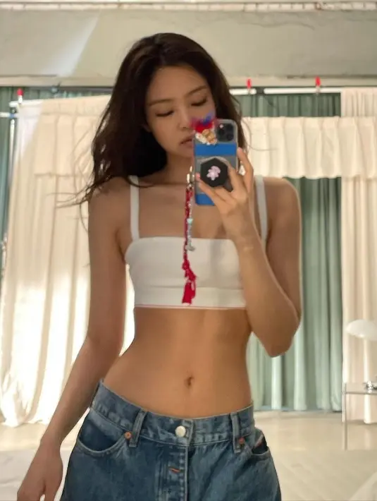 Jennie mengenakan jeans berpinggang rendah untuk menonjolkan pinggang mungilnya.  Dengan atasan putih crop top spangetti strapnya. (@jennierubyjane)