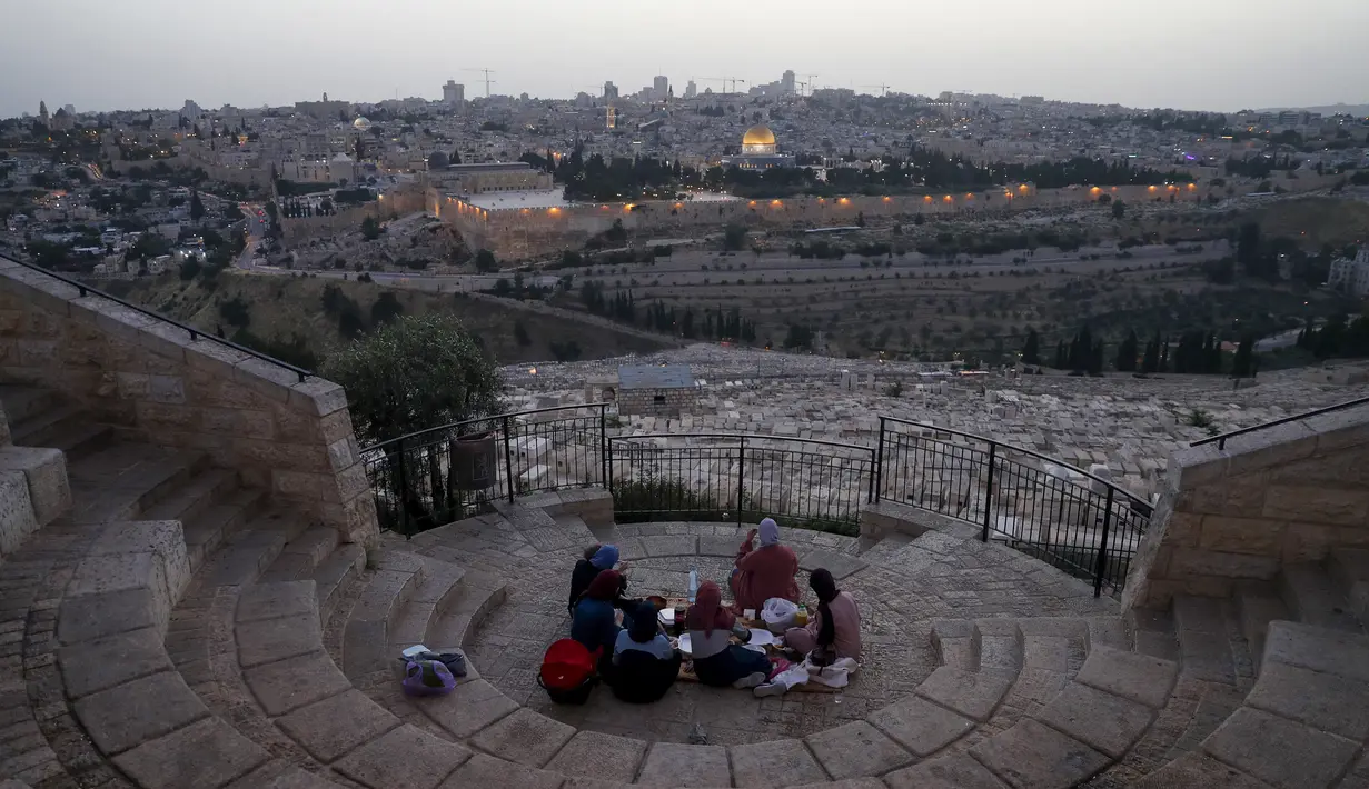 Warga Palestina berkumpul untuk berbuka puasa selama bulan suci Ramadan dengan latar belakang Kota Tua Yerusalem dan kompleks Masjid al-Aqsa yang ditutup selama krisis pandemi coronavirus di Bukit Zaitun (19/5/2020). (AFP/Ahmad Gharabli)