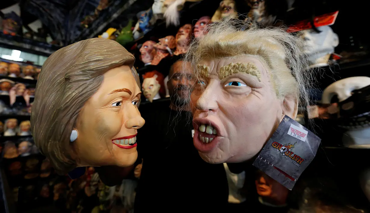 Seorang karyawan memegang topeng yang menggambarkan calon presiden Demokrat Hillary Clinton dan calon presiden dari partai Republik Donald Trump untuk menyambut Hallowen disebuah toko mainan di Los Angeles, California, AS (26/10). (Reuters/Mario Anzuoni)