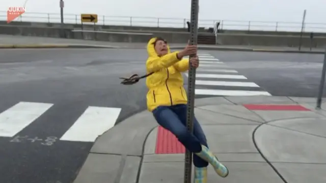 Seorang wanita berusaha sekuat tenaga memegang tiang agar tak terbawa angin topan.