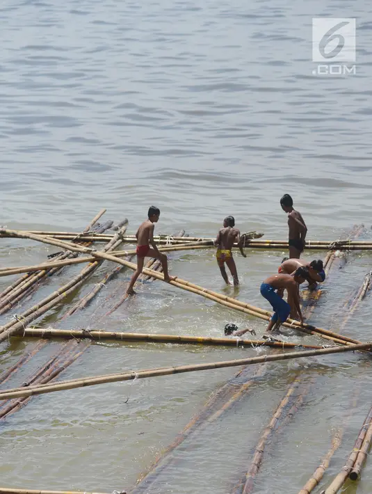 Anak-anak bermain air di atas batang kayu bekas dermaga sandar kapal tradisional di Kawasan Cilincing, Jakarta, Selasa (10/4). Aktifitas bermain laut di pesisir pantai teluk Jakarta ini menjadi keseharian mereka sepeluang sekolah.(Merdeka.com/Imam Buhori)