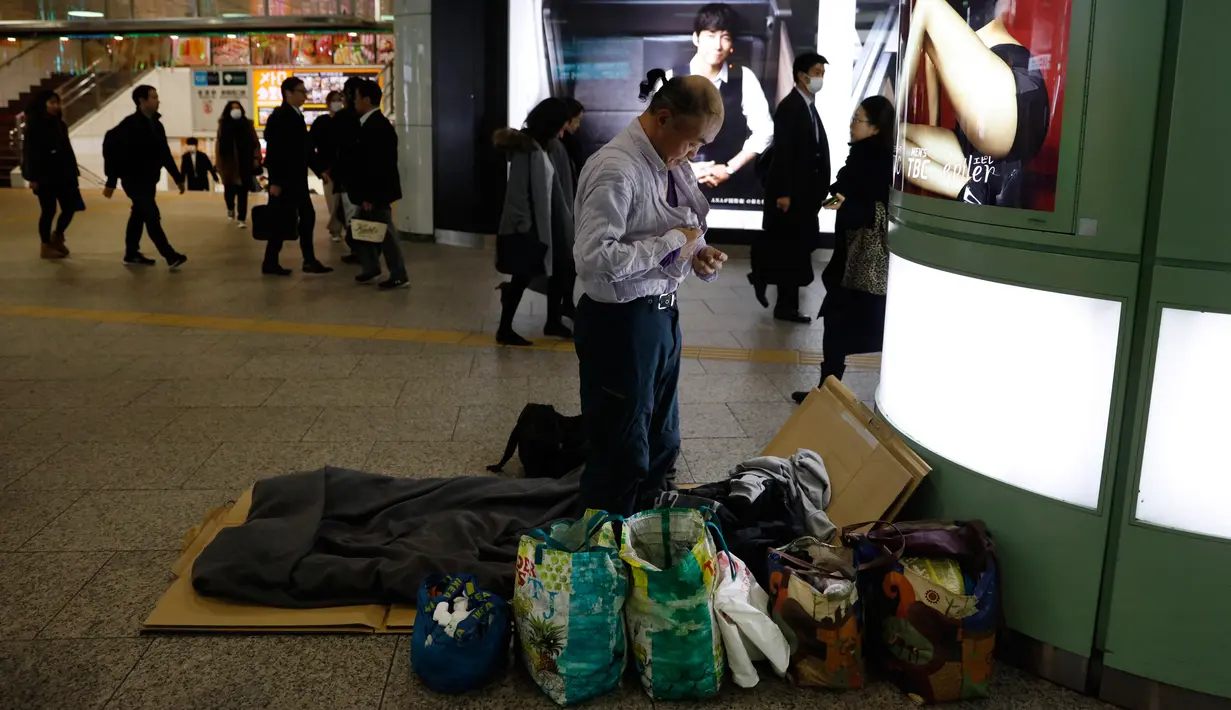 Seorang tunawisma Toshihiro Masuda (59) mengganti pakaian tidur di Stasiun Shinjuku, Tokyo, Jepang, Kamis (9/1/2020). Puluhan tunawisma tidur nyenyak di stasiun kereta bawah tanah Tokyo. (AP Photo/Jae C. Hong)