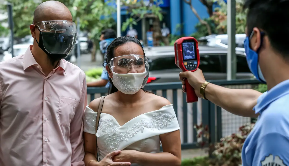 Pasangan mengenakan masker diperiksa suhu tubuhnya dalam "pernikahan massal bermasker" di sebuah taman di Filipina (15/12/2020). Pemerintah Filipina telah memberlakukan kebijakan untuk penggunaan masker di tengah kekhawatiran lonjakan kasus COVID-19 selama musim liburan. (Xinhua/Rouelle Umali)