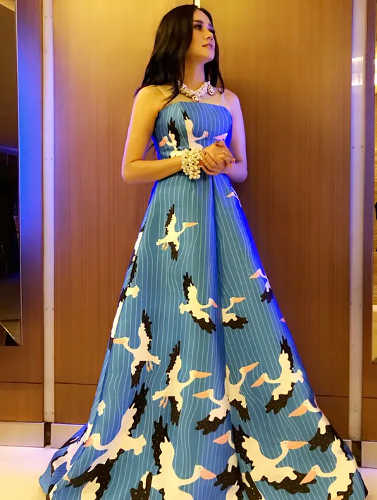 Kali ini Mulan memakai gaun yang panjangnya sampai menjuntai ke lantai. Gaun berwarna biru muda ini bermotif garis-garis dan burung yang berterbangan. Tak lupa aksesoris kalung dan gelang yang senada. (Instagram/mulanjameela1)