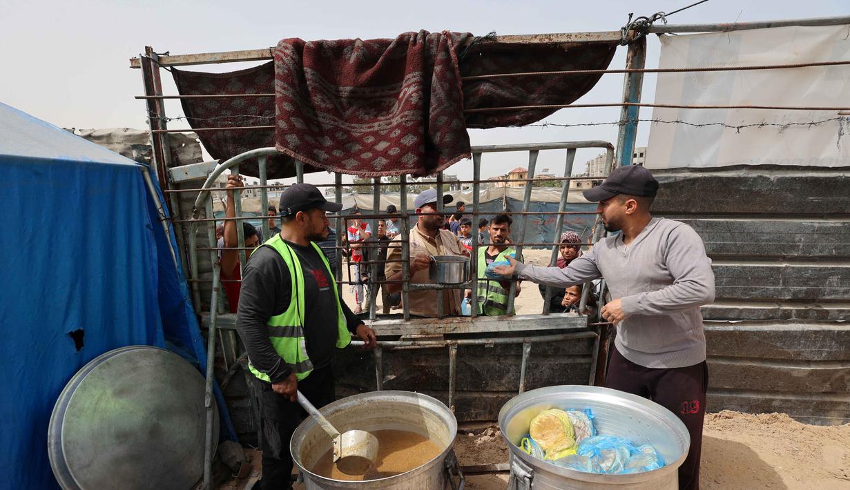 Dua relawan di dapur amal berdiri di dekat panci-panci besar saat mereka membagikan makanan kepada keluarga-keluarga Palestina yang mengungsi di kamp pengungsi Bureij, Jalur Gaza Tengah pada Senin 18 Mei 2026. (Eyad Baba/AFP)