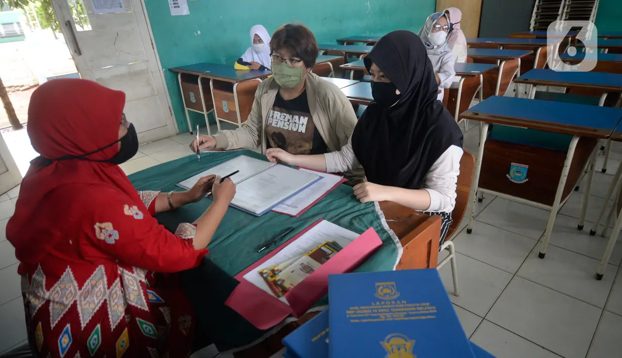 Guru Wali Kelas berdiskusi dengan wali murid saat pembagian raport di SMP Negeri 18 Tangerang Selatan, Banten, Kamis (17/12/2020). Pembagian raport diketahui sedang dilaksanakan sejumlah sekolah.  (merdeka.com/Dwi Narwoko)