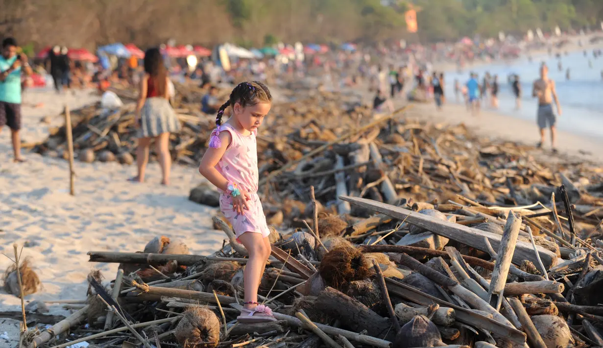 Seorang gadis melintas di atas sampah yang terdampar akibat cuaca buruk di Pantai Kuta, Bali, Jumat (15/2). Sampah bervolume besar kembali menepi di Pantai Kuta, kali ini pesisir pantai berpasir putih itu dipenuhi sampah buah kelapa. (SONNY TUMBELAKA/AFP)