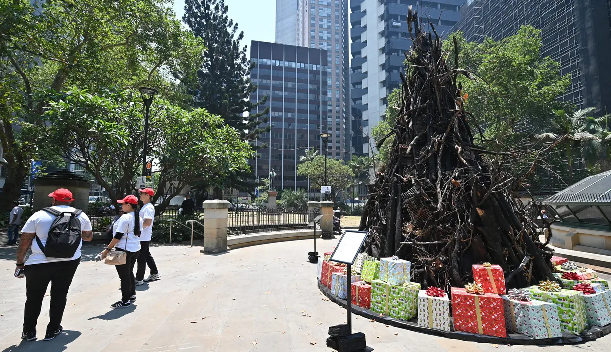 Orang-orang berpose di depan instalasi yang dijuluki 'Pohon Natal yang Terbakar' di Sydney (18/12/2019). Warga Australia di pantai timur bersiap menghadapi "ancaman baru" ketika gelombang panas disertai dengan angin yang bergolak menurunkan lebih dari 100 kebakaran hutan di kawasan itu. (AFP/Peter P
