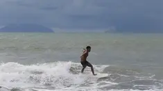 Abu Dzar Al-Ghifari berselancar ketika Gunung Krakatau (kiri) dan Anak Krakatau terlihat di lepas pantai Carita, Banten (26/12). Pemerintah meminta warga menghindari pantai di daerah-daerah tersebut. (AP Photo/Achmad Ibrahim)