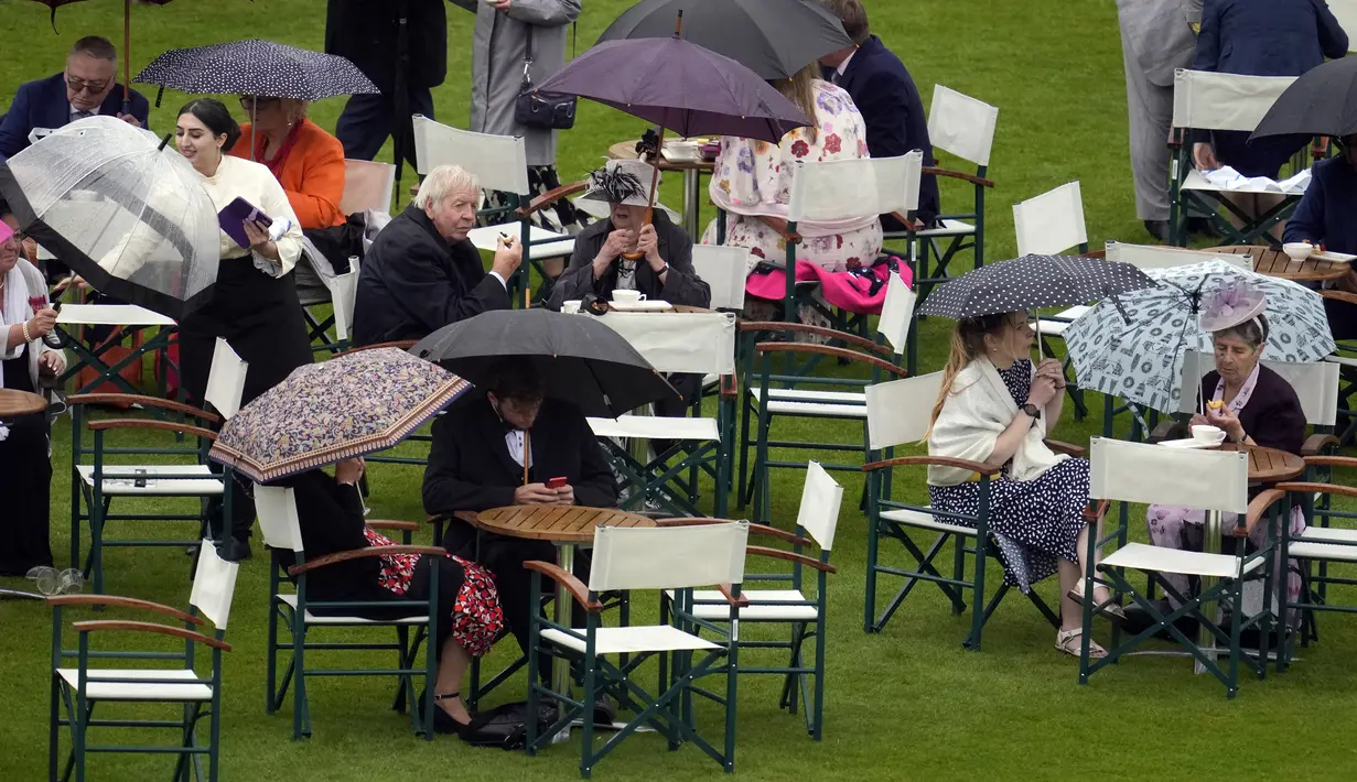 Para tamu berlindung di bawah payung dari hujan saat mereka duduk di meja saat menghadiri pesta kebun pertama musim ini di Istana Buckingham, London, Inggris, 11 Mei 2022. Pesta kembali untuk pertama kalinya sejak 2019 setelah wabah virus corona COVID-19. (AP Photo/Matt Dunham, Pool)