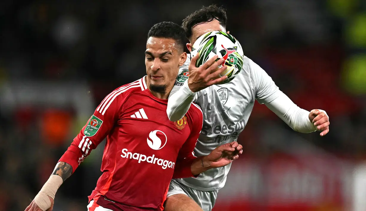 Pemain Manchester United, Antony (kiri) berebut bola dengan pemain Barnsley, Corey O'Keeffe pada laga Carabao Cup 2024/2025 di Old Trafford, Manchester, Inggris, Rabu (18/09/2024) WIB. (AFP/Paul Ellis)