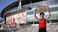 Seorang penggemar Arsenal berdiri dengan memegang spanduk anti Liga Super Eropa di luar Stadion Emirates, London, Senin (19/4/2021). (Foto: AFP/Tolga Akmen)