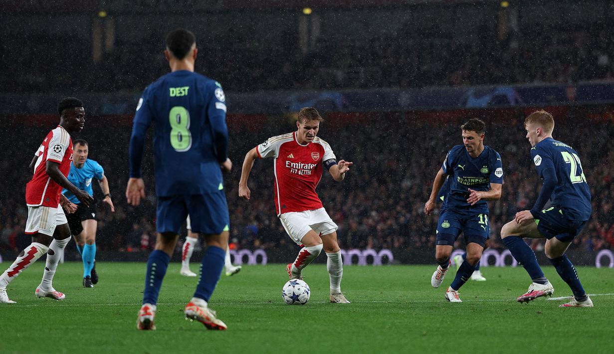 Pemain Arsenal, Martin Odegaard (tengah) berusaha melewati adangan dari sejumlah pemain PSV Eindhoven pada laga Grup B Liga Champions 2023/2024 di Emirates Stadium, London, Kamis (21/09/2023) dini hari WIB. (AFP/Adrian Dennis)