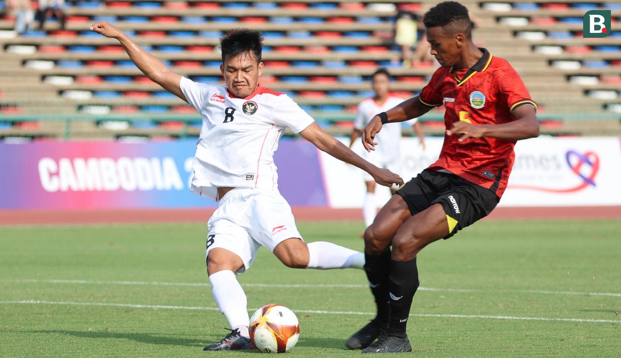 <p>Pemain Timnas Indonesia U-22, Witan Sulaiman (kiri),&nbsp;menendang bola dibayangi pemain Timor Leste, Cristevao Moniz Fernandes pada pertandingan ketiga Grup A SEA Games 2023 yang berlangsung di Olympic Stadium, Phnom Penh, Kamboja, Minggu (7/5/2023). (Bola.com/Abdul Aziz)</p>