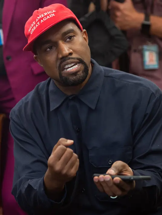 Rapper Kanye West ketika bertemu dengan Presiden AS, Donald Trump di Oval Office, Gedung Putih, Kamis (11/10). West mengenakan topi bertuliskan slogan yang kerap digaungkan Trump, yakni "Make America Great Again". (SAUL LOEB / AFP)