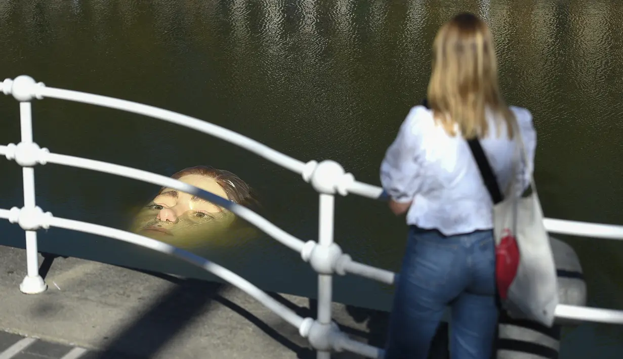 Seorang wanita melihat patung Bihar karya seniman hiperrealis asal Meksiko Ruben Orozco yang terendam di Sungai Nervion, Kota Bilbao, Basque, Spanyol, 14 Oktober 2021. Saat pasang surut, sosok fiberglass seberat 120 kg tersebut terendam dan terlihat setiap hari. (ANDER GILLENEA/AFP)