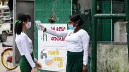 Seorang guru mengenakan masker mengukur suhu tubuh siswa di gerbang sekolah saat hari pendaftaran sekolah di Yangon, Myanmar  (13/7/2020). Myanmar sejak Selasa (7/7) memulai pendaftaran sekolah untuk tahun ajaran 2020-2021, yang tertunda akibat pandemi COVID-19. (Xinhua/U Aung)