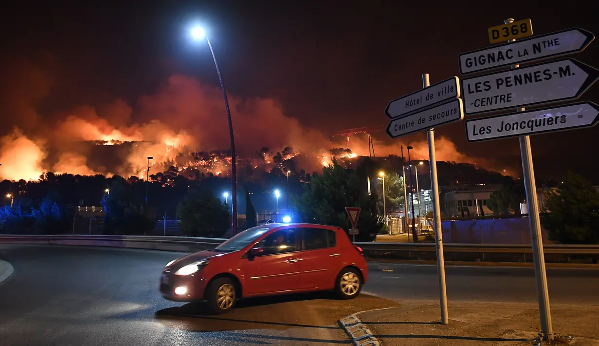 Sebuah mobil melintas saat kebakaran hutan di Les Pennes-Mirabeau, dekat Marseille, Prancis, Kamis (11/8). Penyebaran api hingga melahap habis 2.260 hektare lahan. (AFP PHOTO/BORIS HORVAT)
