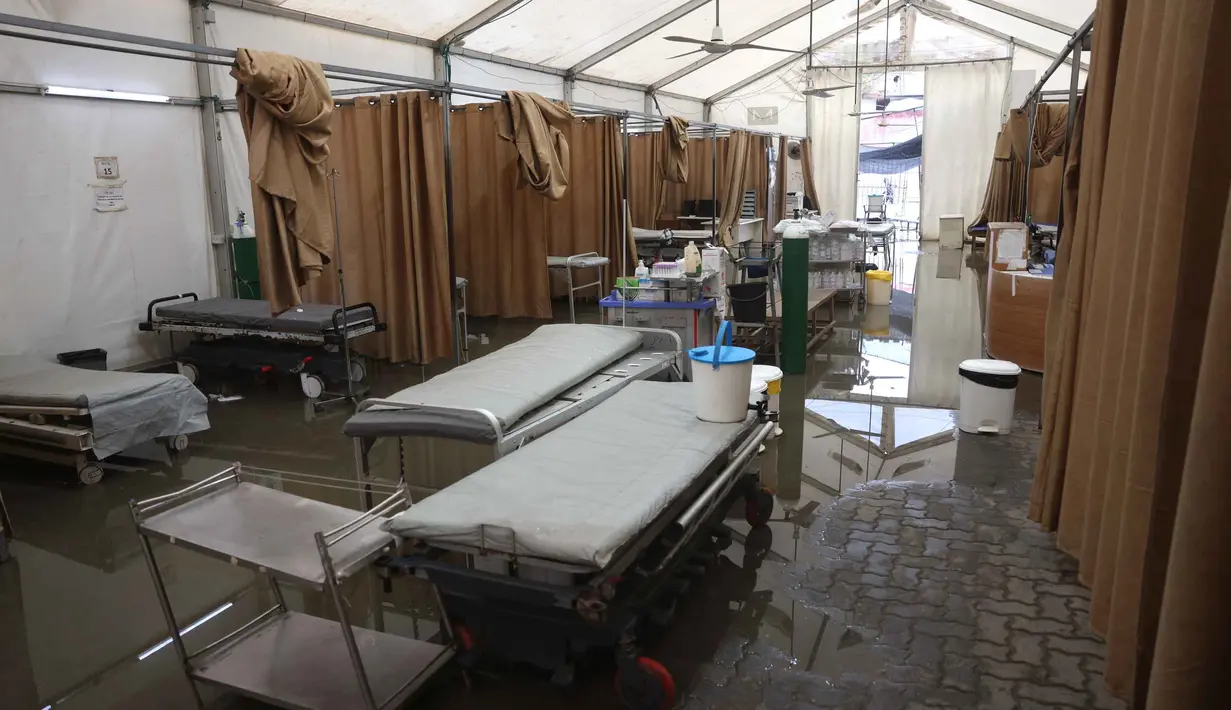 Imbasnya, layanan Instalasi Gawat Darurat (IGD) di tenda tersebut ditutup sementara. Tampak dalam foto, ranjang-ranjang kosong di dalam tenda darurat milik Rumah Sakit Nasser, yang berfungsi sebagai tempat penerimaan pasien rawat jalan dan departemen gawat darurat, setelah hujan lebat di Khan Yunis di Jalur Gaza selatan pada 26 Maret 2026. (Bashar Taleb/AFP)