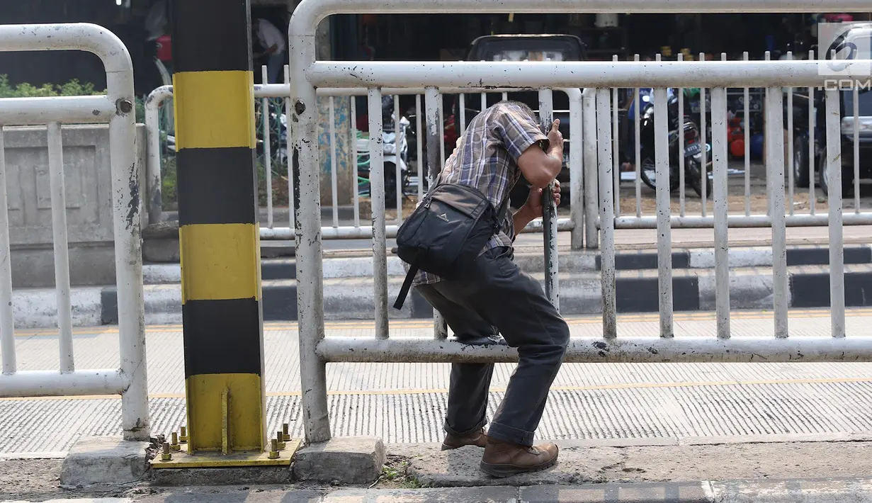 Seorang pria memanfaatkan pagar pembatas jalan untuk menyeberang di Pasar Minggu, Jakarta, Kamis (5/4). Jembatan Penyeberangan Orang (JPO) yang tak kunjung diperbaiki membuat warga menyeberang lewat celah pagar pembatas. (Liputan6.com/Immanuel Antonius)