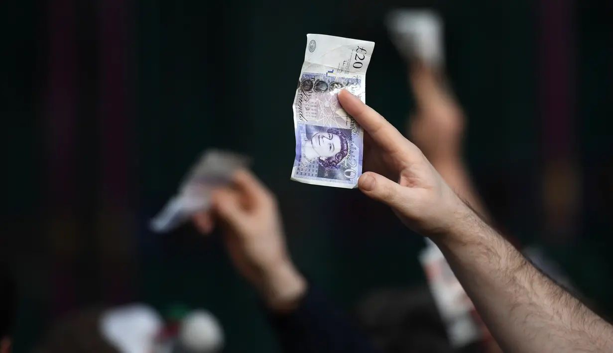 Seorang pembeli memegang uang selama lelang daging menyambut malam Natal di Smithfield Market, London, Selasa (24/12/2019). Dalam tradisi yang hadir sejak 1800-an, calon pembeli bisa menawar harga daging tersebut.  (DANIEL LEAL-OLIVAS / AFP)