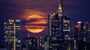 Bulan purnama muncul dari balik gedung-gedung di kawasan perbankan di Frankfurt, Jerman, 14 Juni 2022. Fenomena ini disebut juga sebagai Strawberry Supermoon karena terjadi pada saat panen strawberry.  (AP Photo/Michael Probst)