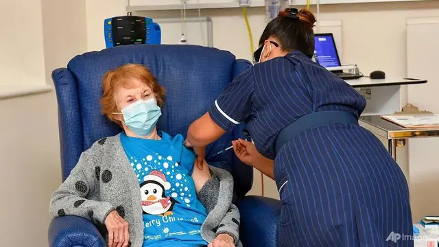 Margaret Keenan, 90 tahun, pasien pertama di Inggris yang menerima vaksin Pfizer-BioNTech COVID-19, diberikan oleh perawat May Parsons di University Hospital, Coventry, Inggris, 8 Des 2020. (Jacob King / Pool via AP)