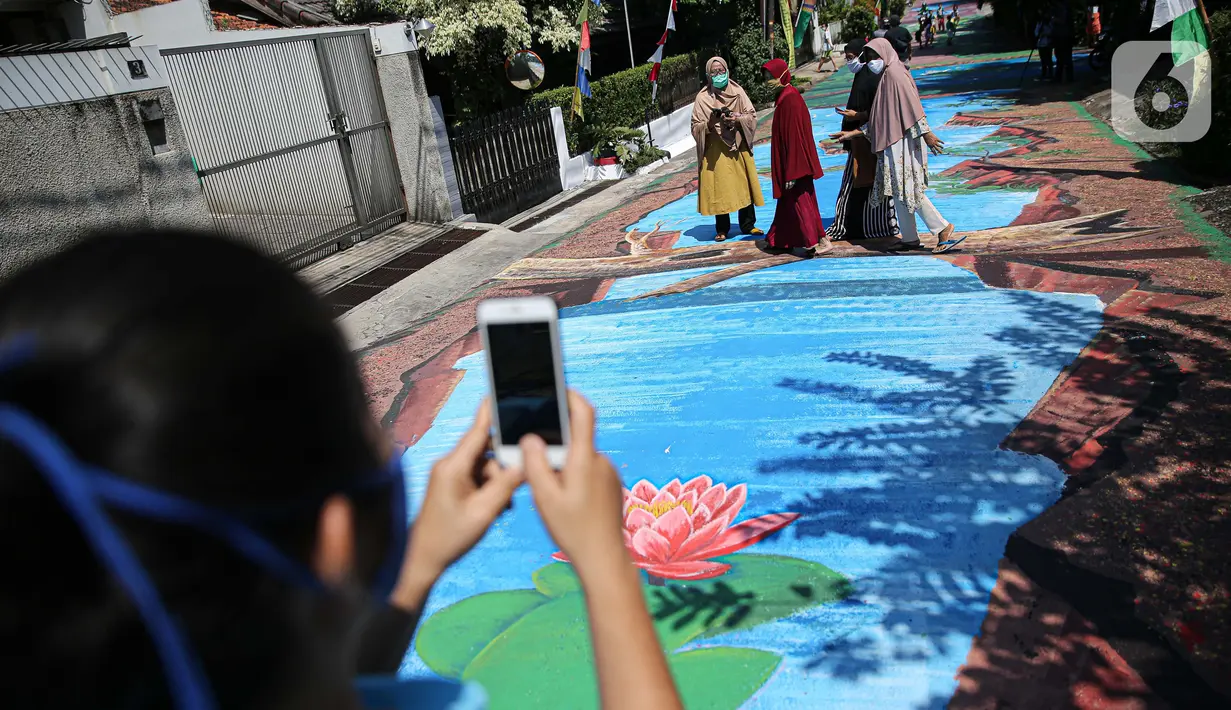 Warga berfoto di atas jalan yang telah dilukis mural di Jalan Keuangan, Cilandak, Jakarta, Rabu (26/8/2020). Museum Basoeki Abdullah bekerjasama dengan Perupa Jakarta Raya membuat mural dengan memanfaatkan ruang publik di sepanjang jalan menuju museum Basoeki Abdullah. (Liputan6.com/Faizal Fanani)