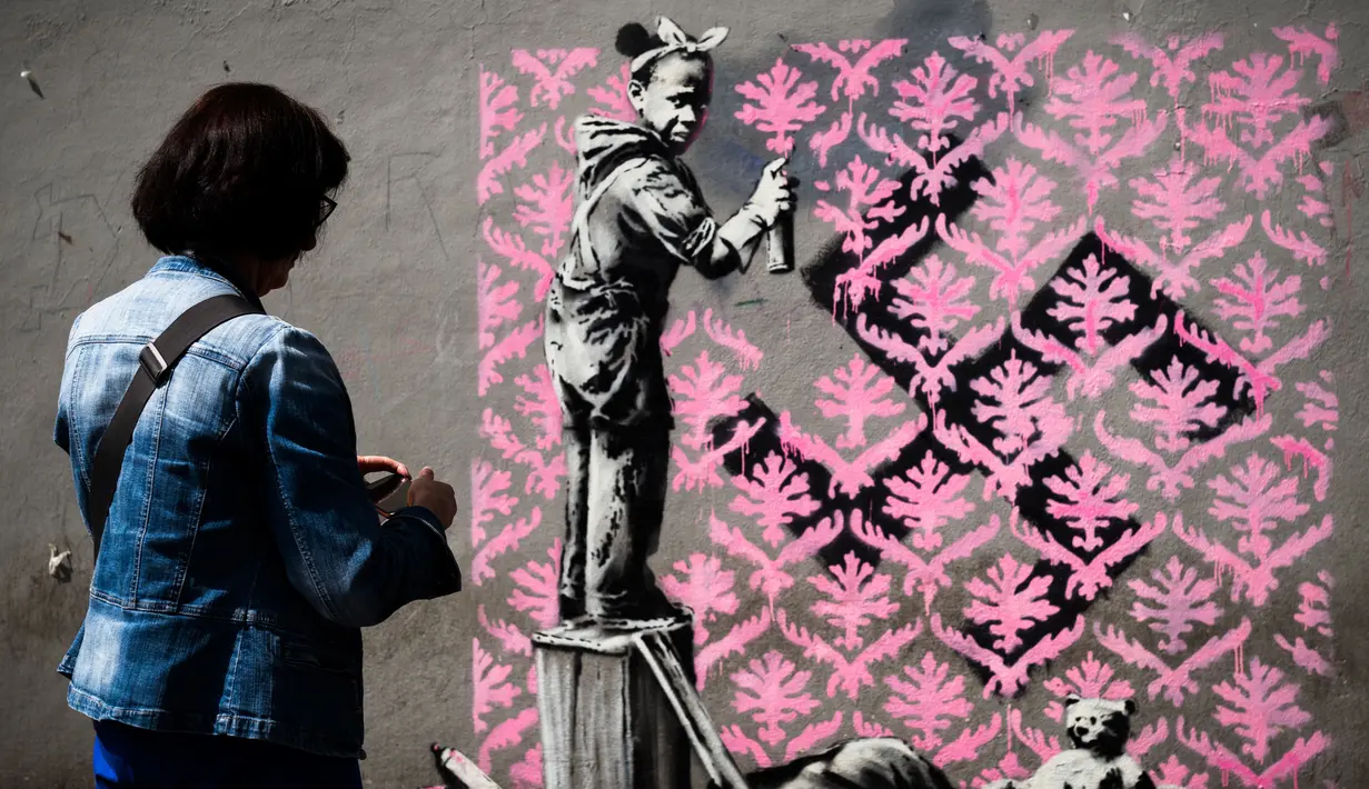 Seorang wanita melihat foto usai mengambil gambar mural yang diduga karya seniman sekaligus aktivis Banksy di Paris, Prancis, Minggu (24/6). Banksy terkenal dengan seni mural luar ruangan. (PHILIPPE LOPEZ/AFP)