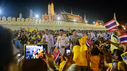 Raja Thailand Maha Vajiralongkorn dan Ratu Suthida menyapa pendukungnya di luar Grand Palace di Bangkok setelah memimpin upacara keagamaan di sebuah kuil Buddha di dalam Istana Raja pada Minggu (1/11/2020). (Jack TAYLOR / AFP)