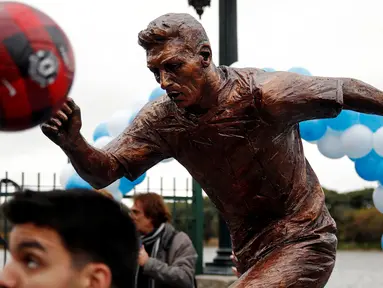 Seorang anak bermain bola di depan patung perunggu Lionel Messi yang baru diresmikan di pusat kota Buenos Aires, Argentina, Selasa (28/6). Patung tersebut guna membujuk Messi membatalkan keputusan pensiun yang sudah diambilnya. (REUTERS/Marcos Brindicci)