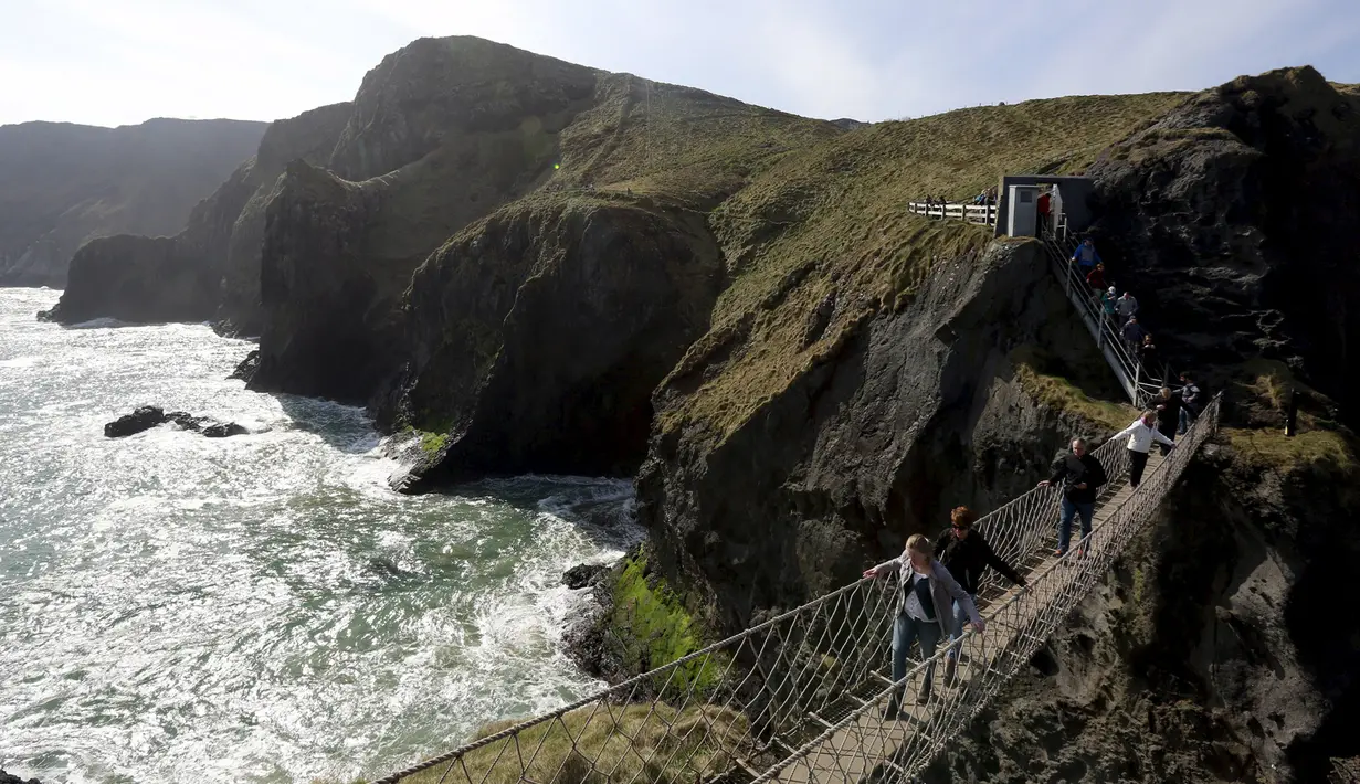 Sejumlah wisatawan mencoba melintasi jembatan Carrick-a-Rede Rope di Pantai Causeway, Irlandia Utara, Rabu (8/4/2015). Jembatan tersebut diperkirakan telah dibangun selama lebih dari 350 tahun oleh para nelayan salmon. (REUTERS/Cathal McNaughton)