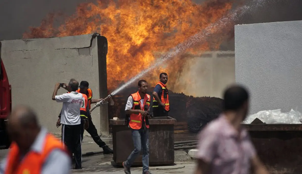 Beberapa petugas pemadam kebakaran Palestina berusaha memadamkan api di gudang PBB setelah serangan militer Israel di barat kota Gaza, (12/7/2014). (AFP PHOTO/Mahmud Hams)