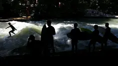 Sejumlah peselancar melihat rekannya menaklukkan ombak buatan saat bermain surfing di sungai 'Eisbach' di taman English Garden di Munich, Jerman (24/6/2019). Sungai Eisbach merupakan salah satu tempat berselancar sungai yang paling populer di Munich. (AP Photo/Matthias Schrader)